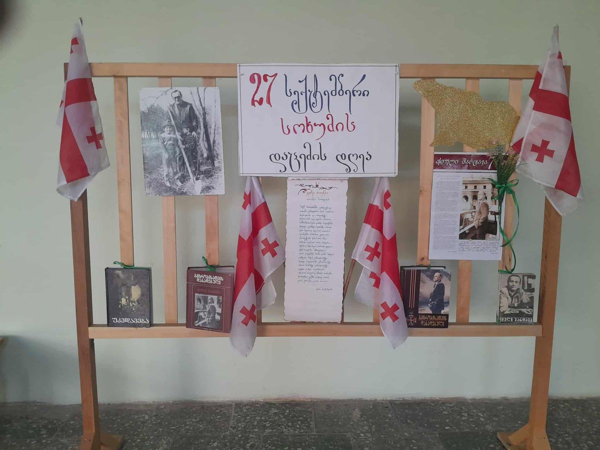 სკოლის სტენდი „27 სექტემბერი — სოხუმის დაცემის დღე“, ქართულ დროშებით, ფოტოებითა და წიგნებით